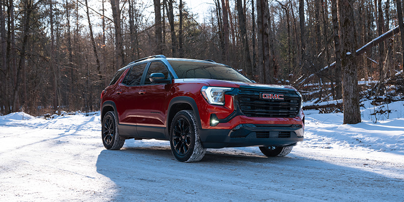 2025 GMC Terrain SUV in red driving on a snowy forest road, highlighting its rugged performance, modern design, and all-wheel-drive capability in winter conditions.