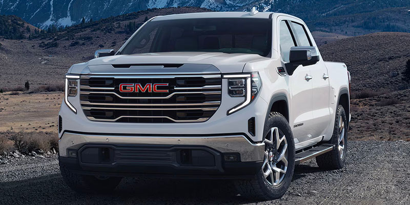 Exterior of a white GMC Sierra 1500 truck showing the front and driver's side, parked near a mountain.