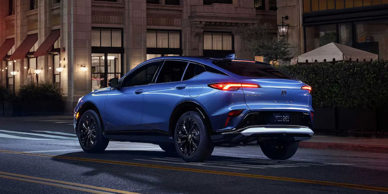 Blue compact crossover driving through a city street at night with illuminated taillights and upscale urban surroundings.