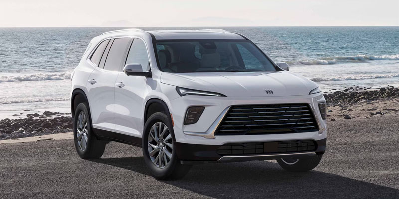 A white Buick SUV parked near the beach with the ocean in the background.