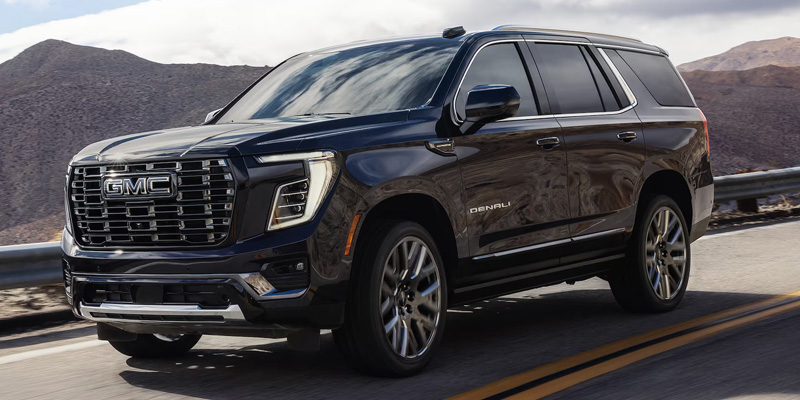Black GMC Yukon Denali SUV driving on a scenic mountain road showcasing its bold exterior design.