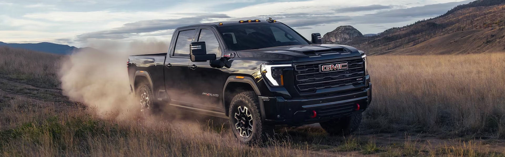 Black GMC pickup truck driving through a dusty off-road landscape with mountains in the background.