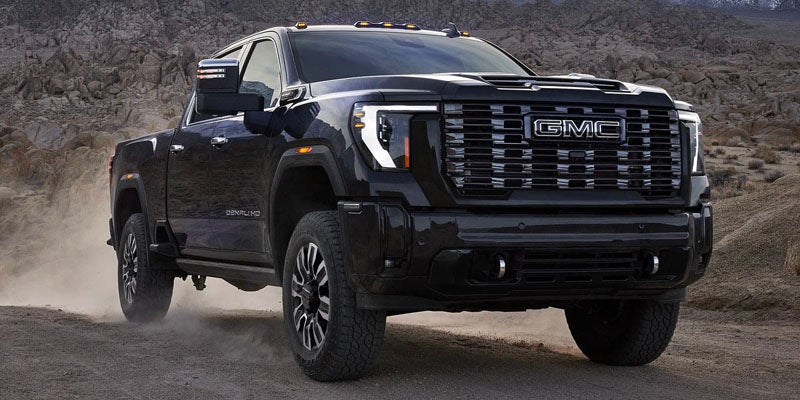 Black GMC pickup truck driving through a dusty off-road landscape with rugged terrain in the background.