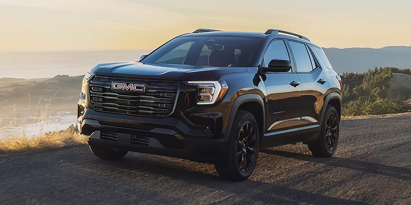Black SUV parked outdoors on a scenic road with sunlight and a landscape background.
